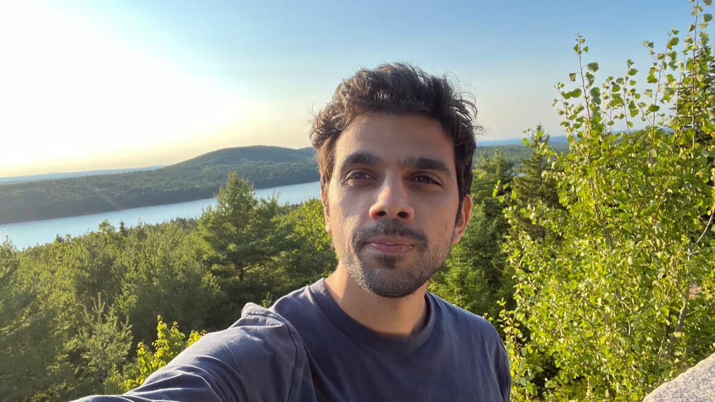 Arun Singh, founder of share/artifacts, outdoors above a lake and forest